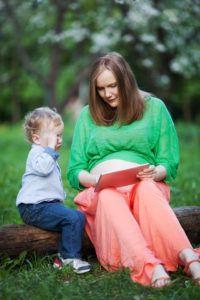 Pregnant mother with little son using touch pad in the park